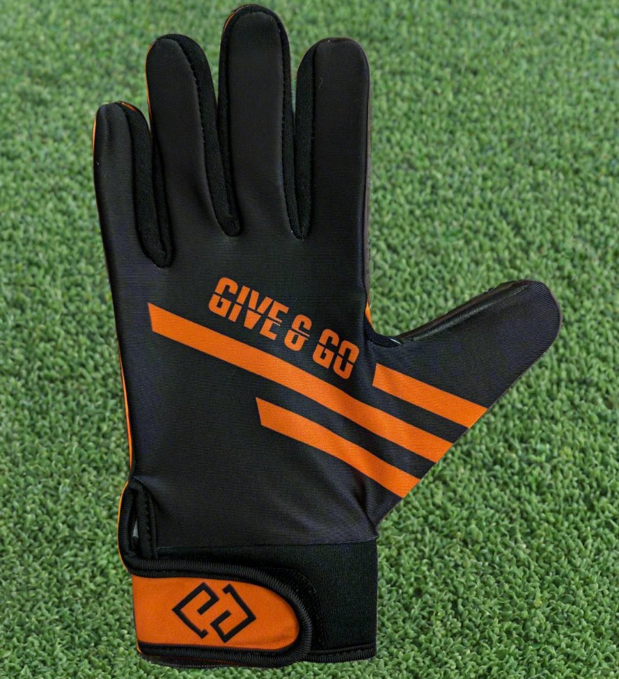 Black and orange GiveAndGo gloves on a green grass background