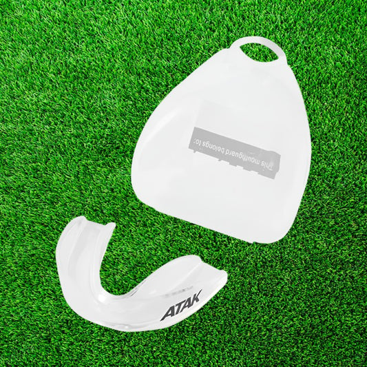 White mouthguard with 'ATAK' branding on a green grass background