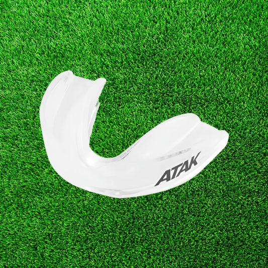 White mouthguard with 'ATAK' branding on a green grass background